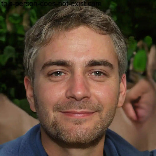 Un homme souriant avec des cheveux courts, grisâtres et une barbe.