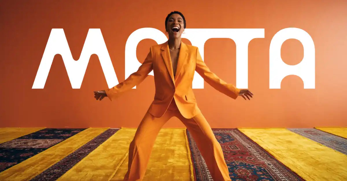 Une personne en tailleur orange avec un large sourire et les bras tendus.