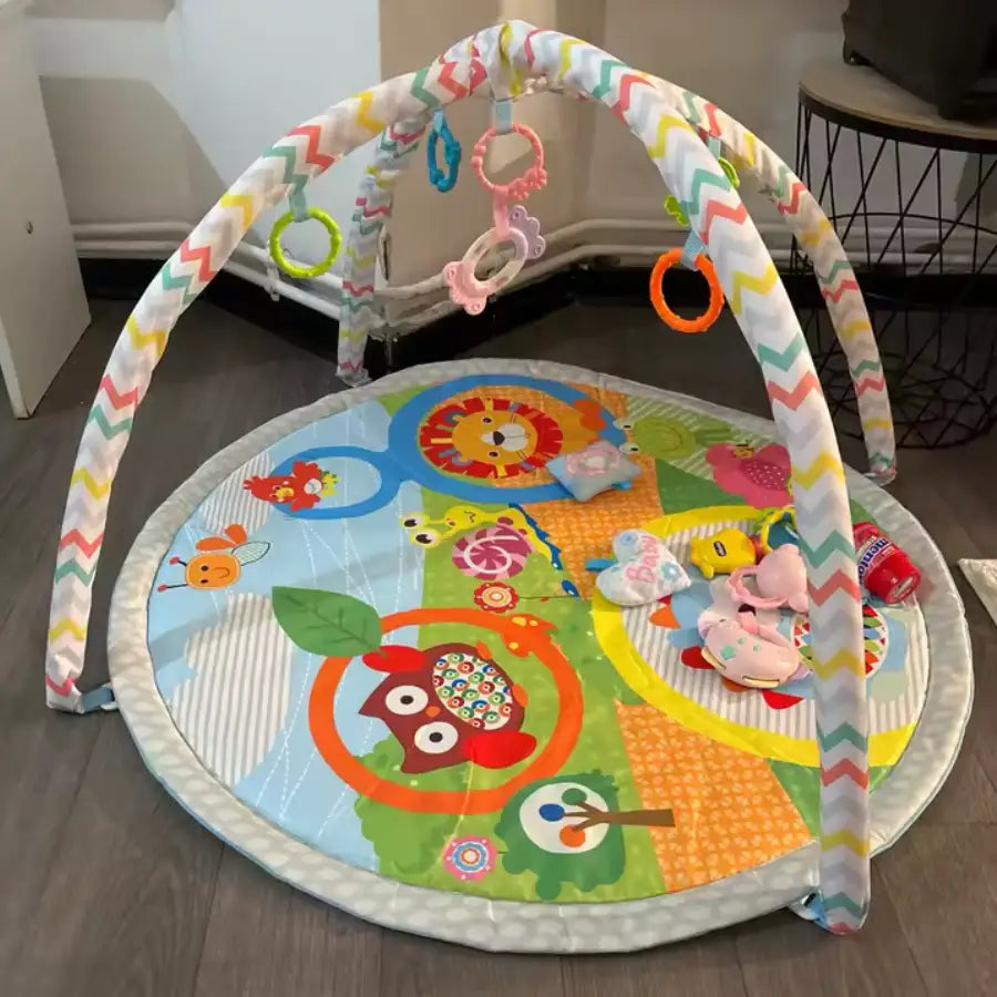 Tapis de jeu pour bébé avec des motifs d’animaux colorés et des jouets suspendus, probablement fabriqué en tissu doux et en mousse.