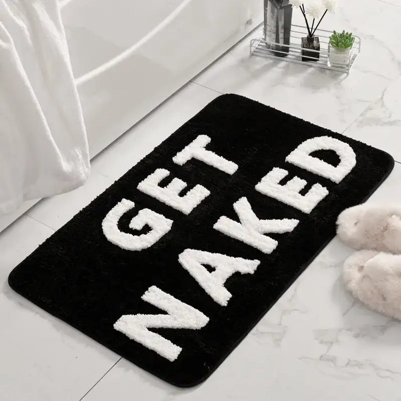 Tapis de bain noir avec le texte blanc « get naked » dans un design audacieux et tridimensionnel.
