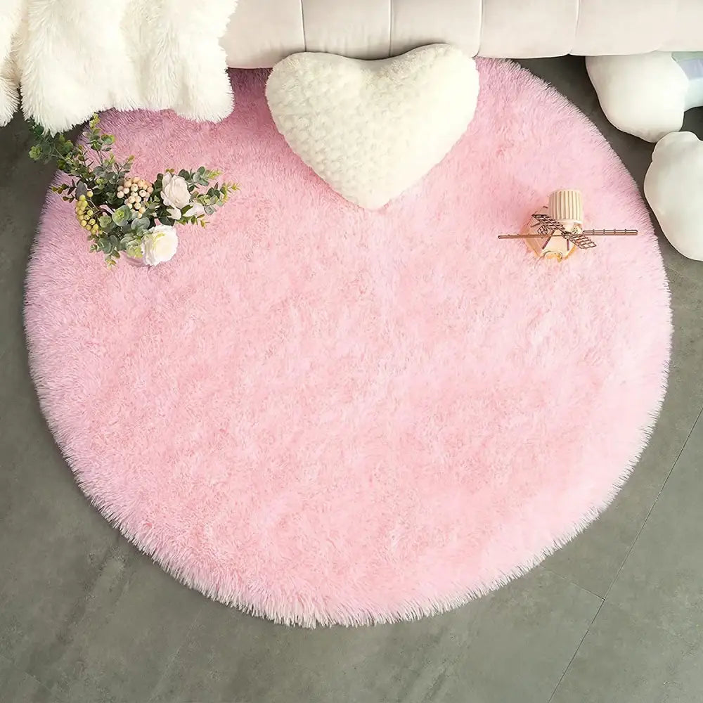 Tapis rose moelleux rond avec coussin en forme de cœur et arrangement floral sur le dessus.