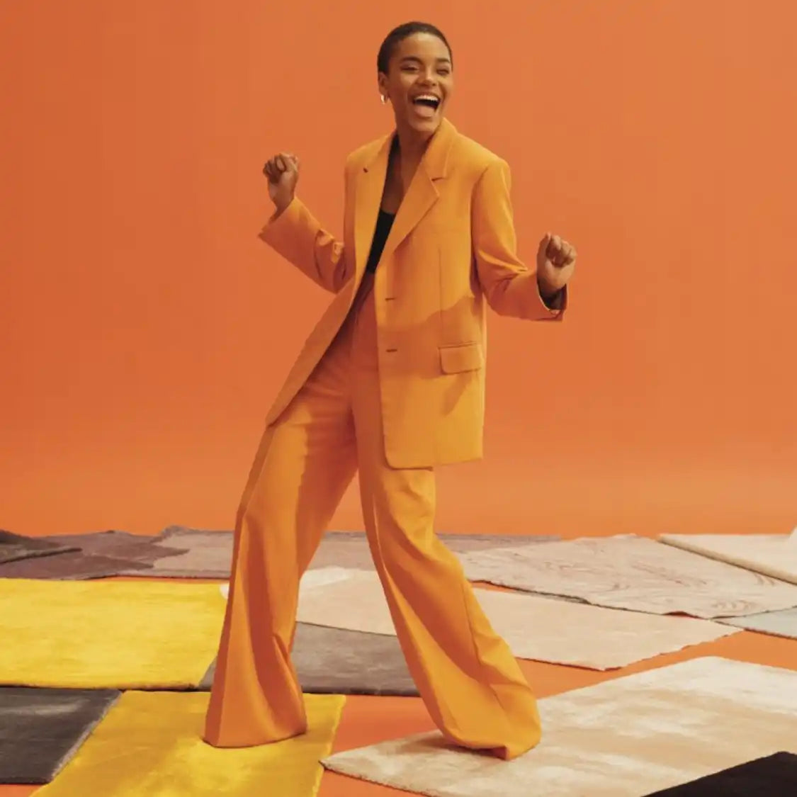 Une femme souriante en costume orange et haut noir.
