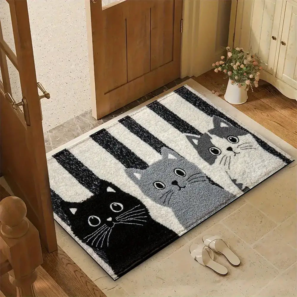 Un tapis de porte rectangulaire moelleux présentant trois chats stylisés en noir, gris et blanc sur un fond de rayures audacieuses noir et blanc.