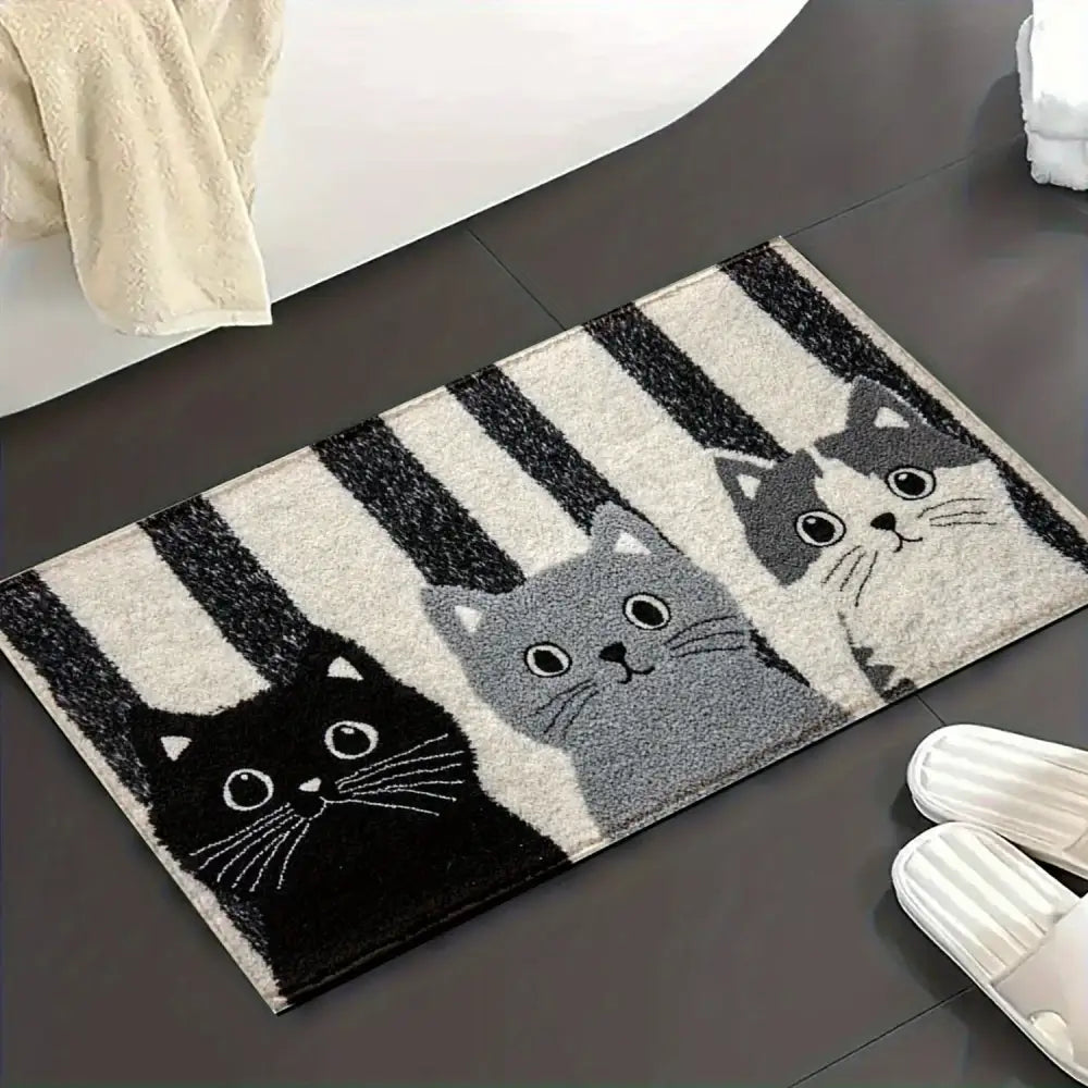 Un tapis de salle de bain moelleux et rectangulaire orné de trois chats de dessin animé en noir, gris et blanc sur un fond de rayures audacieuses noir et blanc.