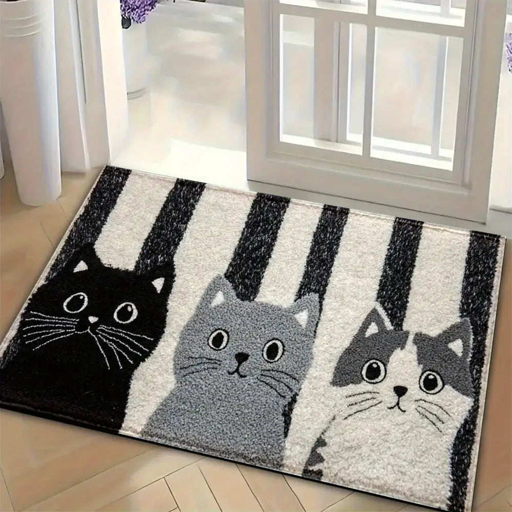 Un paillasson moelleux rectangulaire présentant trois chats de dessin animé en noir, gris et blanc avec un fond rayé.