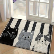 Un paillasson moelleux rectangulaire présentant trois chats de dessin animé en noir, gris et blanc avec un fond rayé.