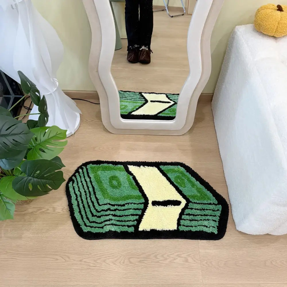 Tapis de bain vert et crème en forme de livre avec une peluche texturée, probablement fabriqué en microfibre ou un matériau similaire.