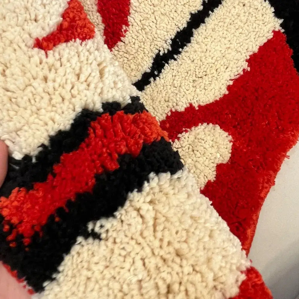Un tapis moelleux à texture avec des motifs géométriques audacieux en rouge, noir et crème.