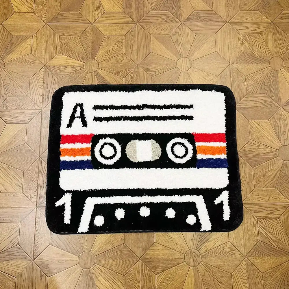 Tapis cassette noir et blanc en tissu pelucheux avec bandes rouges, orange et bleues et support caoutchouc antidérapant