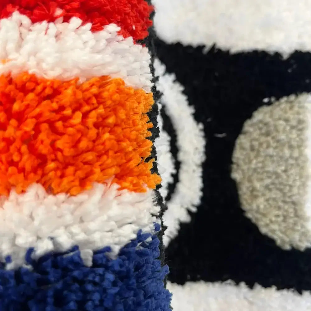 Tapis cassete en tissu texturé avec larges rayures rouges, blanches, orange et bleues sur fond noir à support caoutchouc