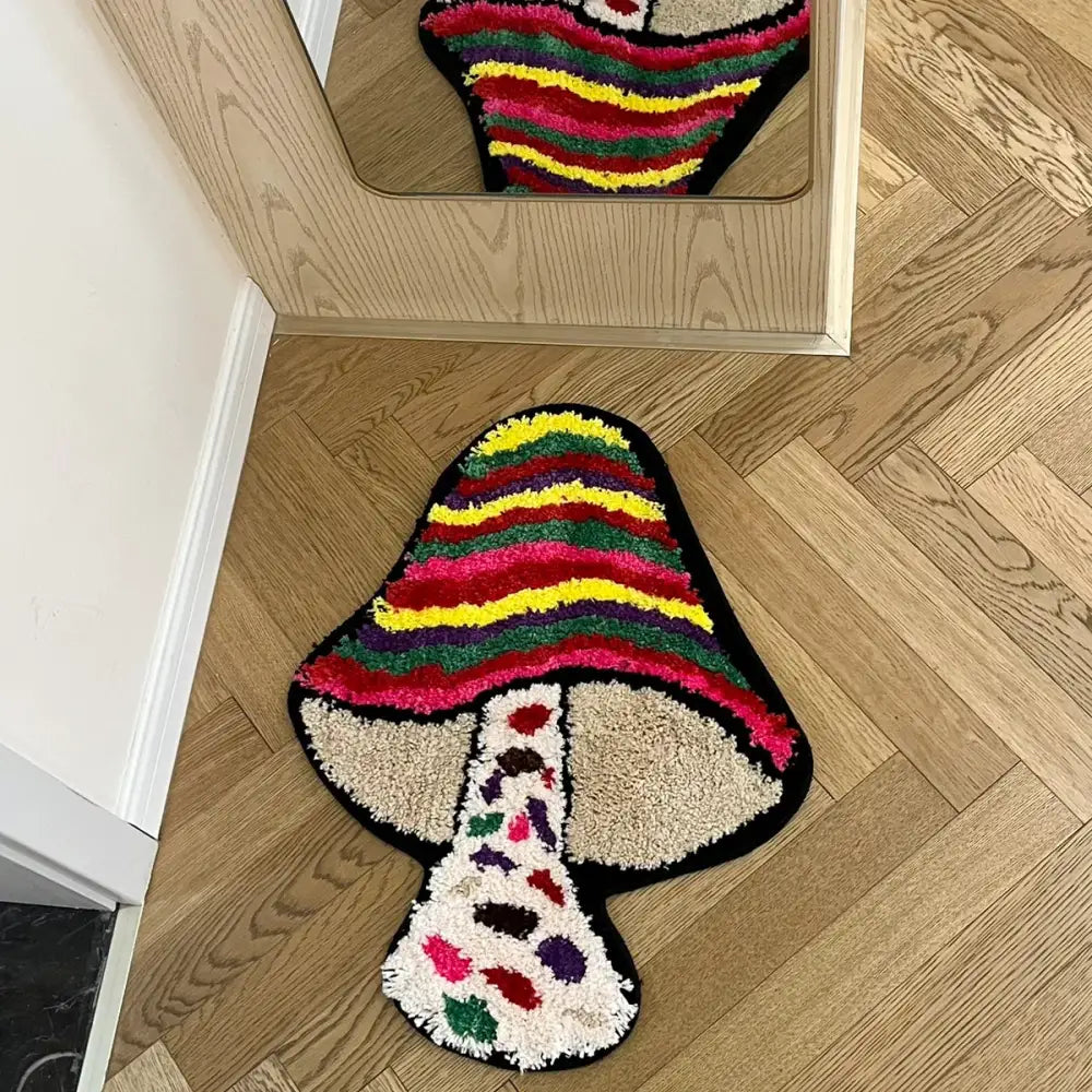 Tapis de bain en forme de champignon multicolore avec motif rayé et détails de feuilles sur un sol en bois, probablement d’Ikea.
