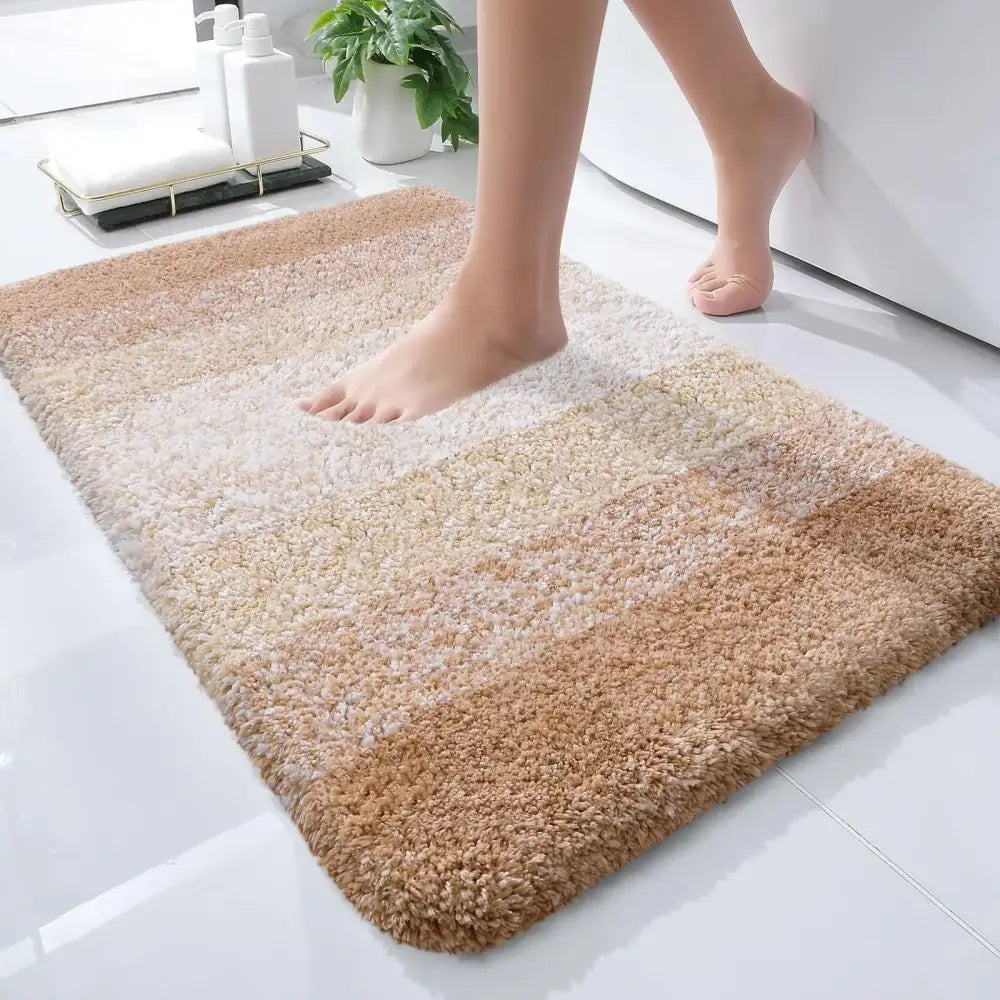 Tapis de bain doux et moelleux en dégradé beige et crème avec une surface texturée et bouclée.