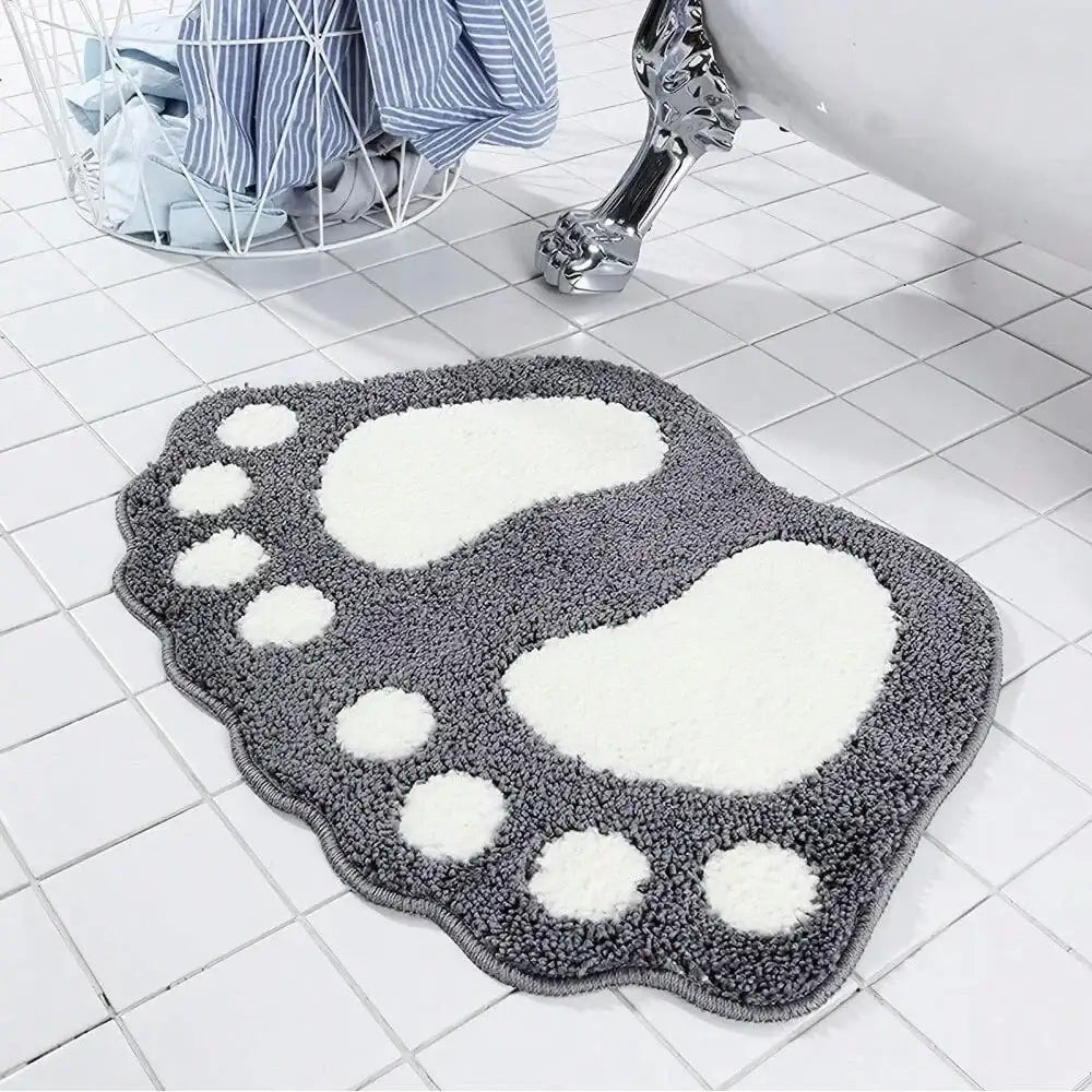 Tapis de bain gris et blanc en forme de pied avec surface texturée, probablement fabriqué en microfibre ou matériau similaire.
