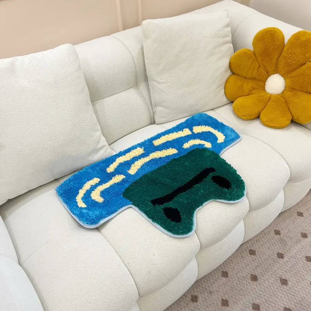 Tapis en peluche bleu et vert en forme de manette de jeu vidéo avec motifs ondulés jaunes.