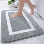 Tapis de bain gris et blanc avec velours texturé, forme rectangulaire, design bordé.