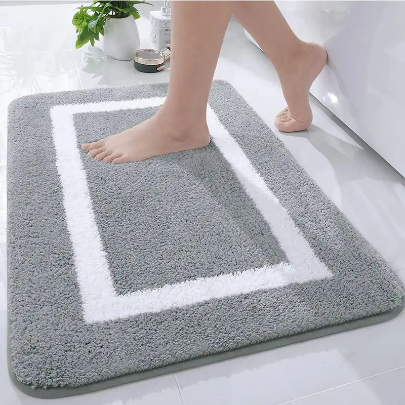 Tapis de bain gris et blanc avec velours texturé, forme rectangulaire, design bordé.