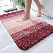 Un tapis de bain moelleux à rayures aux tons de rose et de rouge profond, avec une texture douce et pelucheuse.
