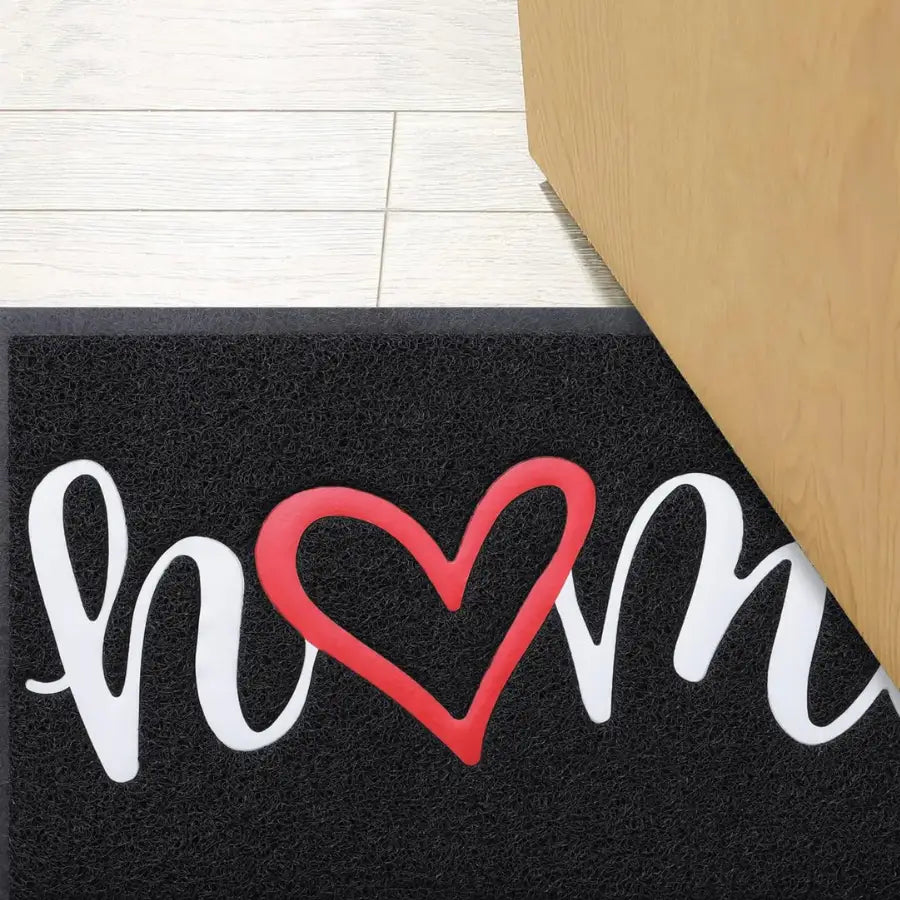 Paillasson en caoutchouc noir avec texte ’home’ en cursif blanc et motif cœur rouge, adapté à un usage intérieur ou extérieur.