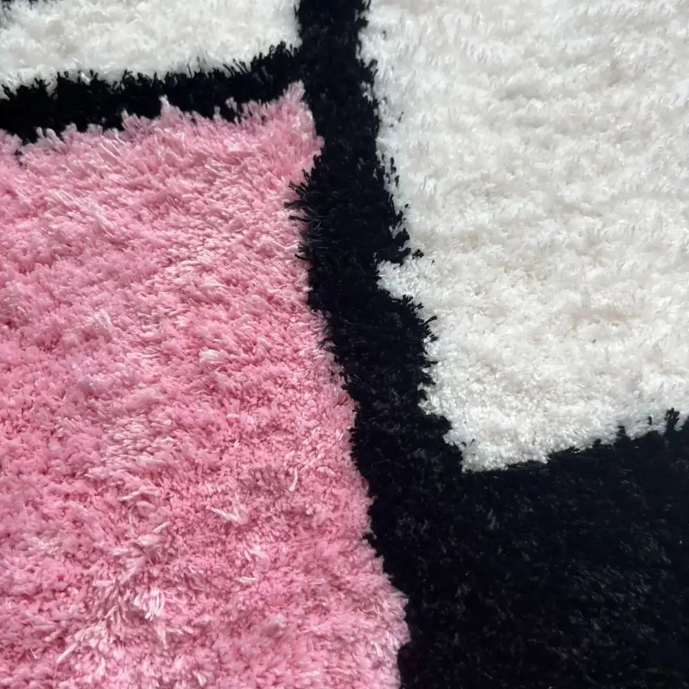 Un tapis moelleux et pelucheux avec un motif géométrique en rose doux, blanc éclatant et sections noir audacieux.