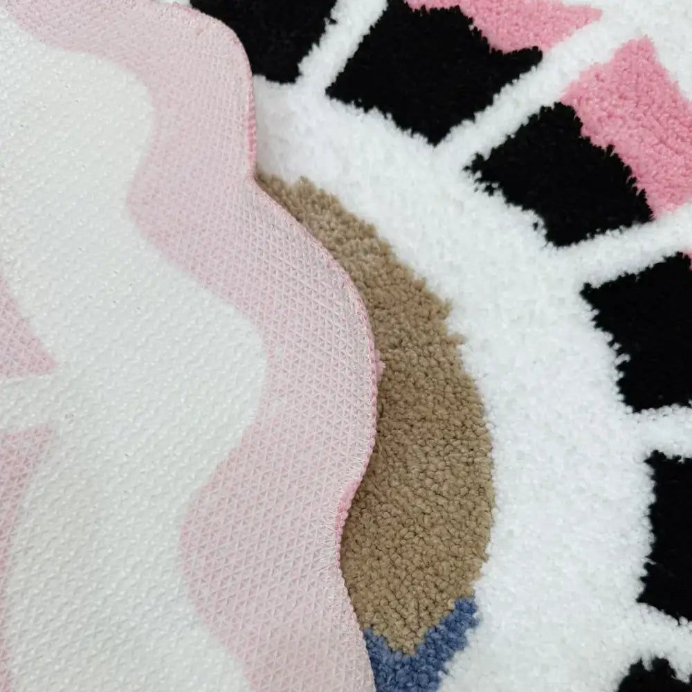 Un tapis moelleux à texture douce avec un design fantaisiste présentant des motifs ondulés rose et blanc aux côtés de formes géométriques noires, beige et bleues.