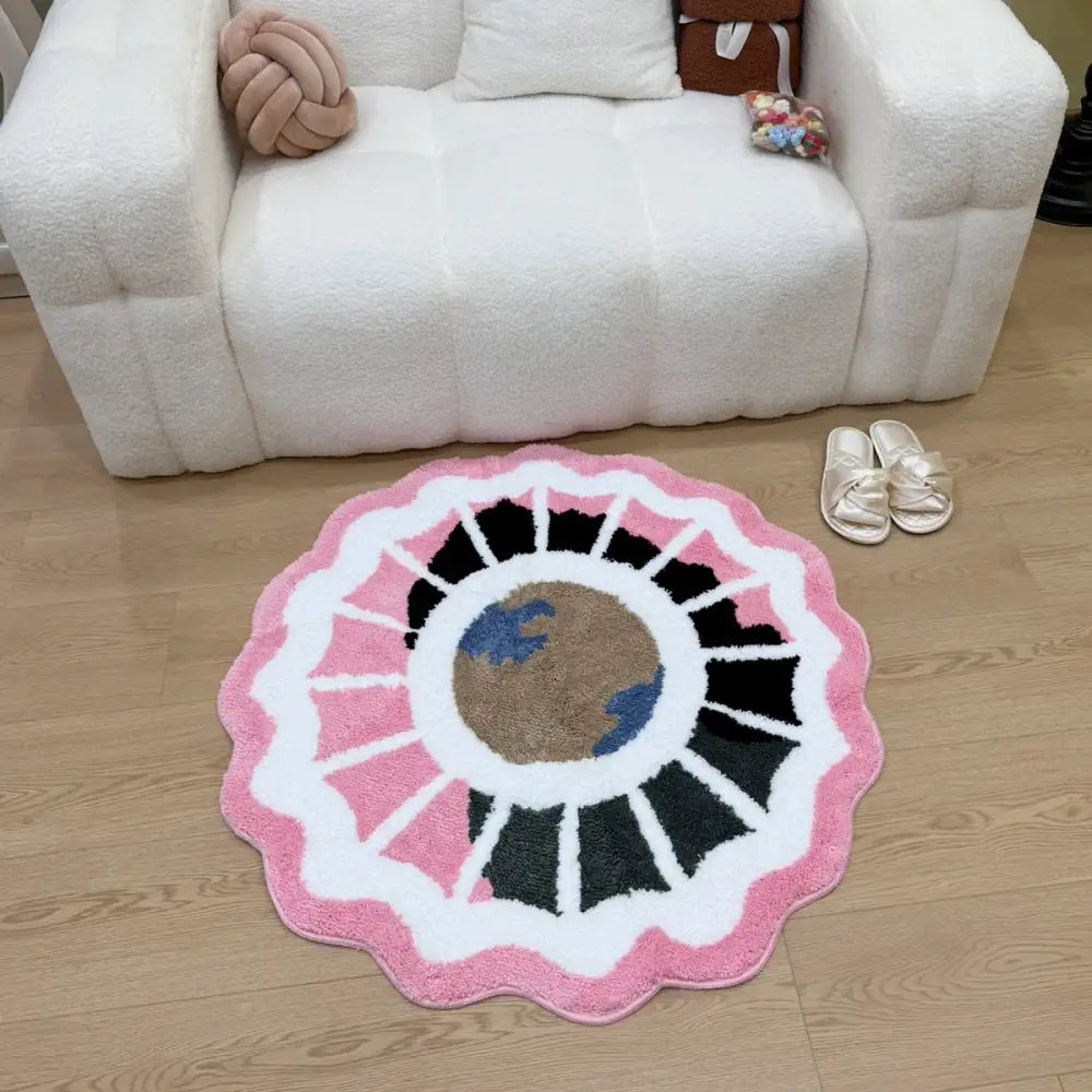 Un tapis moelleux circulaire à bord festonné orné de bordures roses et blanches entourant un motif central de la Terre en marron et bleu.