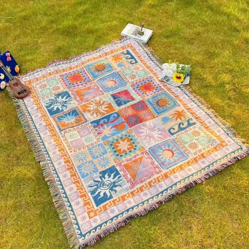 Une couverture en tapisserie tissée colorée présentant un motif patchwork de soleils et de vagues en nuances vives comme l’orange, le bleu, le rose et le vert, avec des bords frangés.