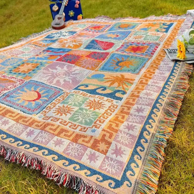 Une couverture jetée patchwork colorée avec des motifs de soleil, vague et géométriques en teintes vives de bleu, orange, rose et vert, ornée de bords frangés.