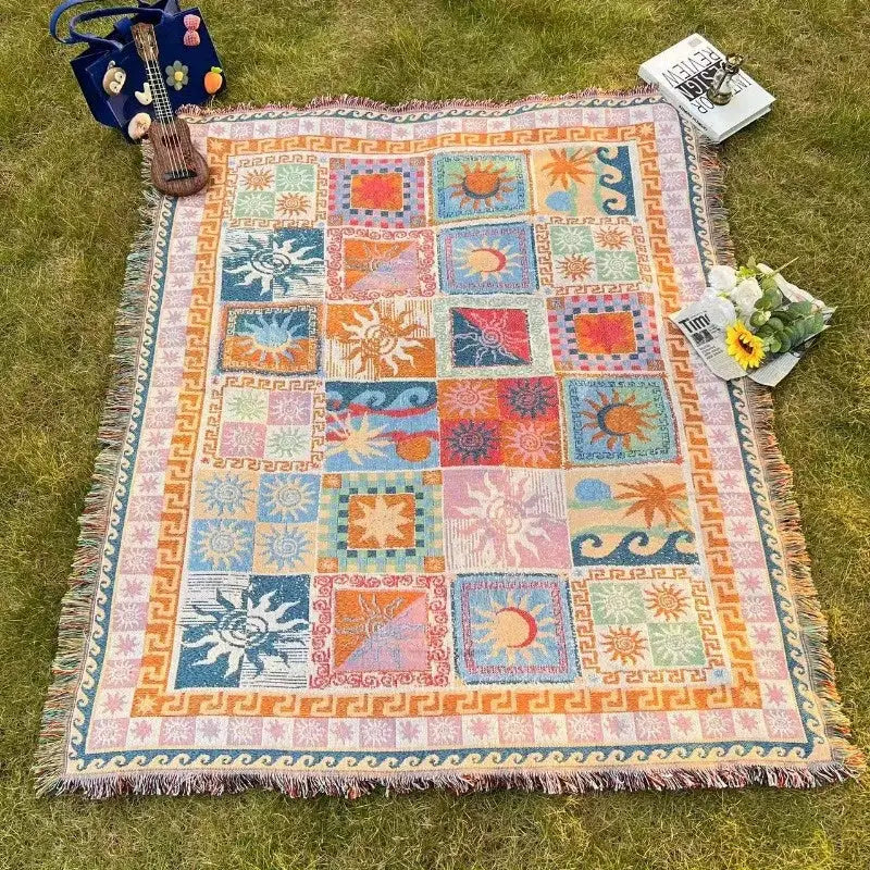 Une couverture jetée patchwork colorée avec des motifs de soleil et de vagues, présentant une texture tissée et des bords frangés.
