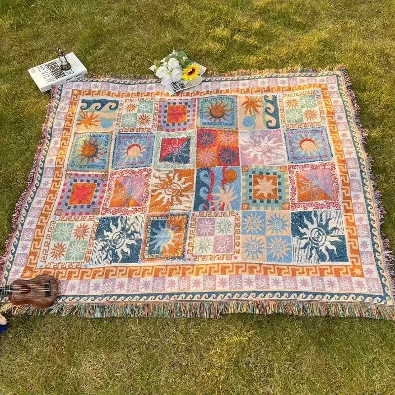 Une couverture tissée en patchwork coloré présentant des motifs vibrants de soleil et géométriques en bleus, oranges, roses et verts avec des bords frangés.
