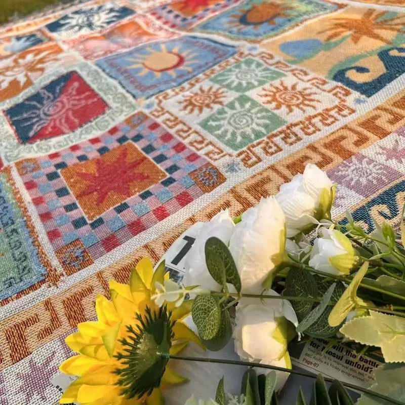Une couverture de pique-nique patchwork colorée avec des motifs solaires et géométriques en nuances vives de rouge, bleu, vert, orange et beige.