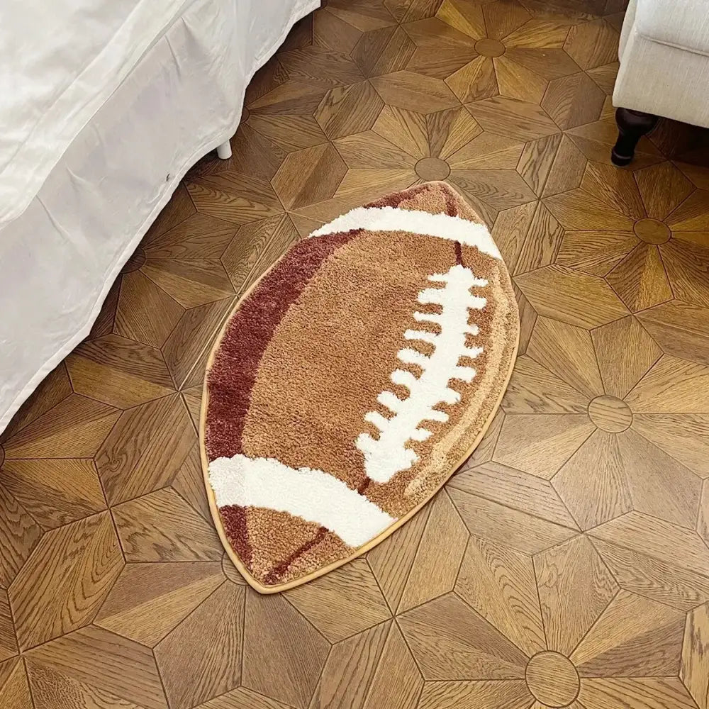 Tapis brun en forme de ballon de football avec des lacets blancs et des accents rouges, probablement fait de matériau moelleux.