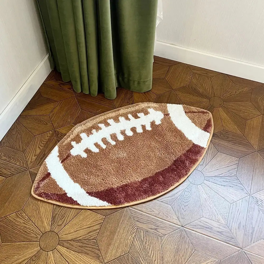 Tapis de bain brun et blanc en forme de ballon de football avec un design texturé de lacets, fabriqué en matériau moelleux.