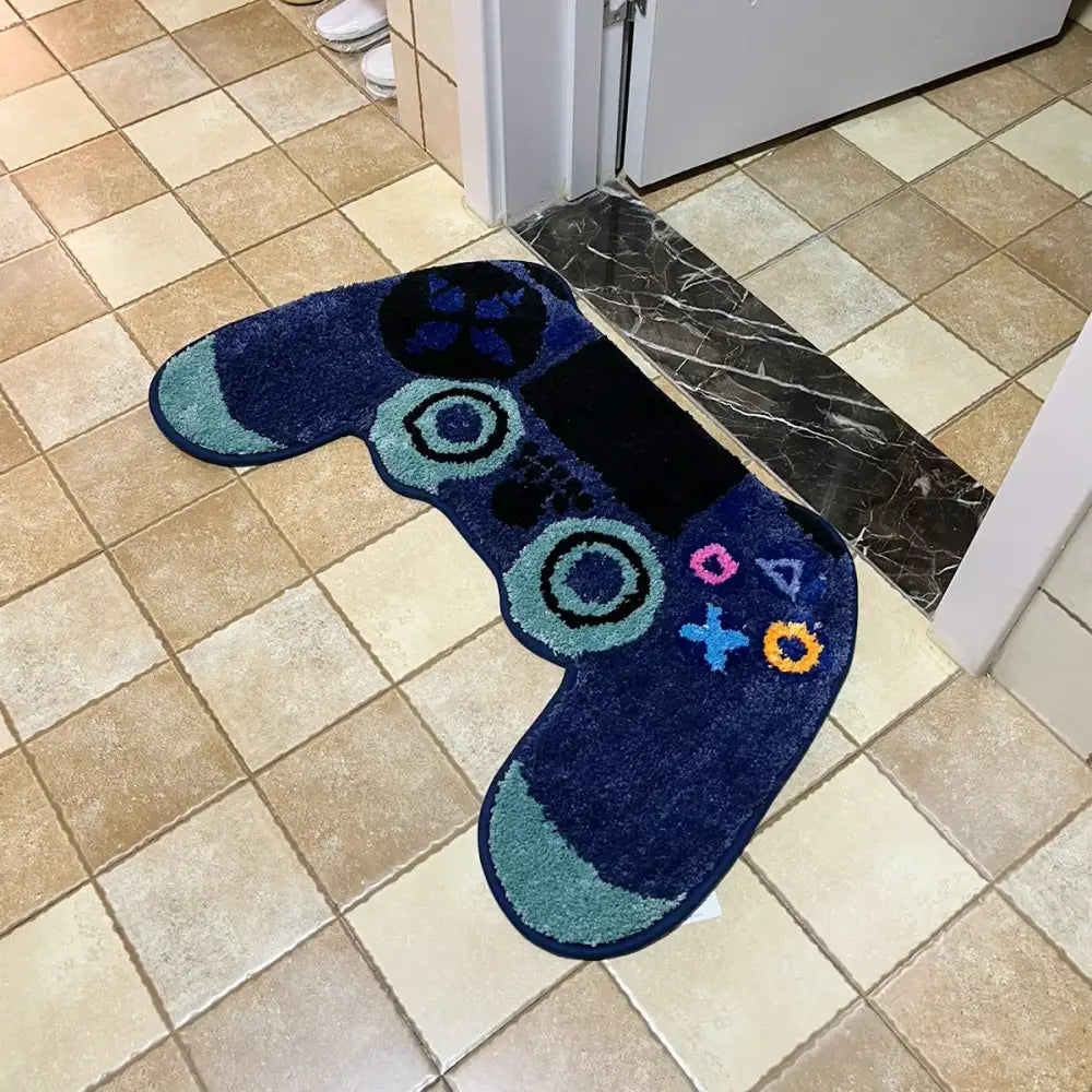 Tapis de bain en forme de manette PlayStation bleue avec des accents blancs et orange, probablement fait de matériau moelleux.