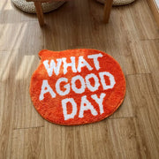 Tapis de bain en peluche orange avec du texte brodé blanc indiquant « quelle belle journée »