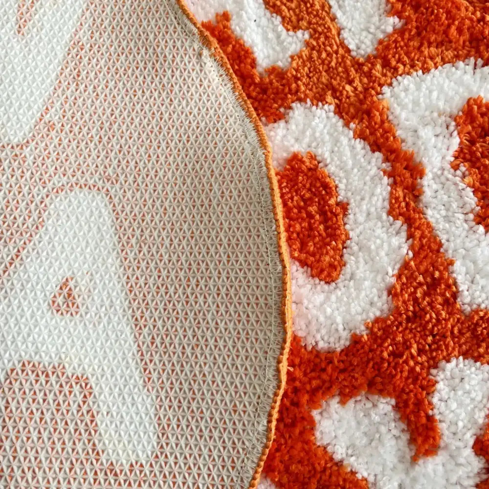 Tapis de bain en peluche à motif orange et blanc avec une surface texturée à boucles.
