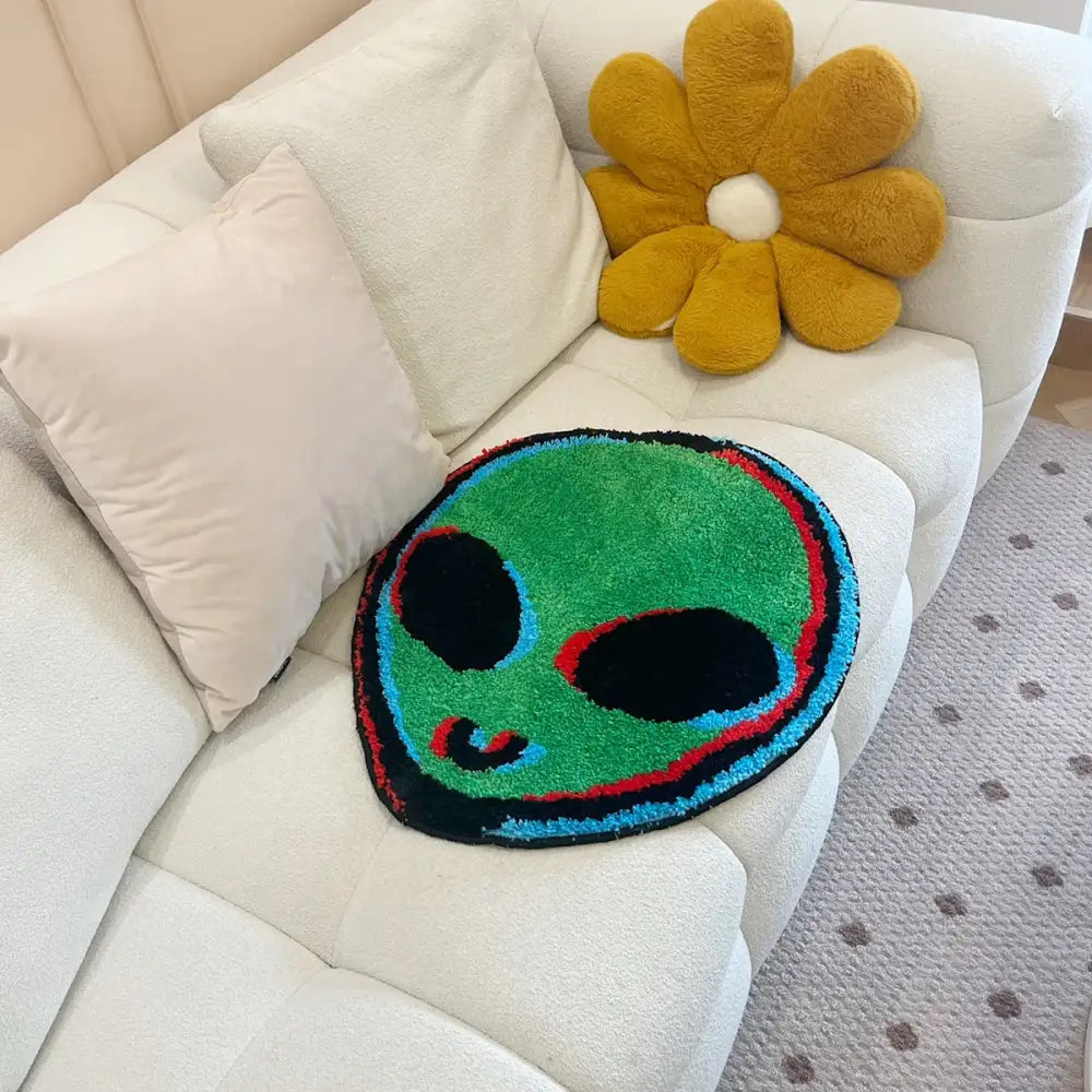 Tapis en forme d’alien vert avec des yeux noirs, des contours rouges et bleus, et une texture duveteuse.