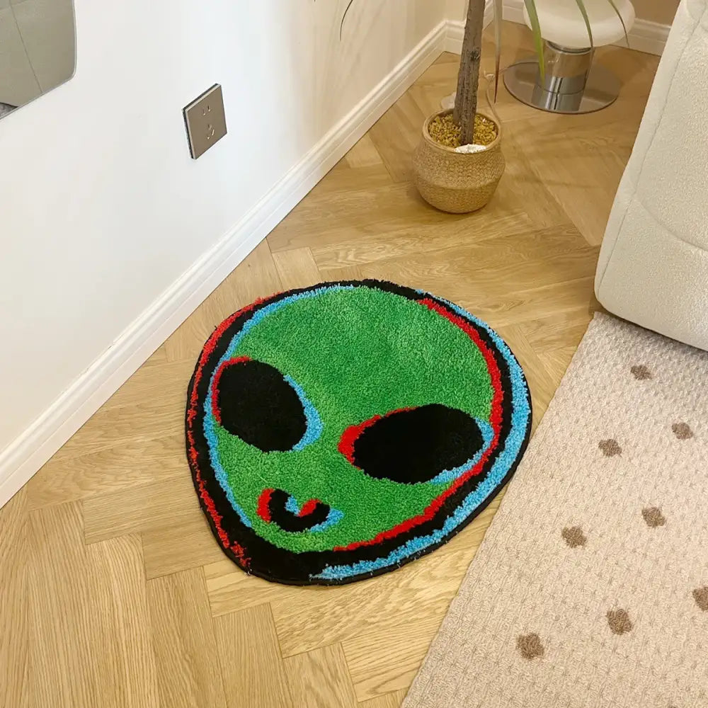 Un tapis rond, moelleux, à thème extraterrestre vert avec des yeux noirs et une bouche souriante soulignée en rouge et bleu.