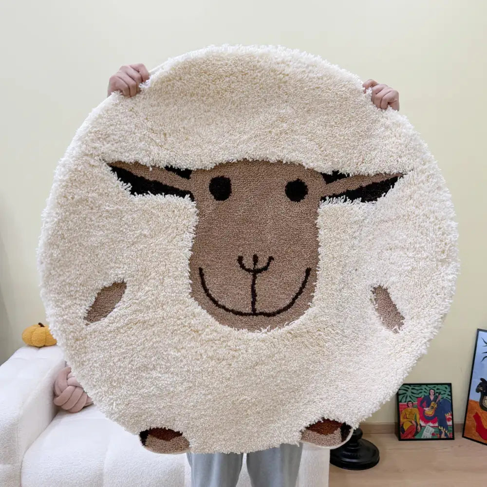 Tapis circulaire moelleux de couleur crème orné d’un design charmant de visage de mouton avec des patches de laine brune pour les oreilles et les joues.