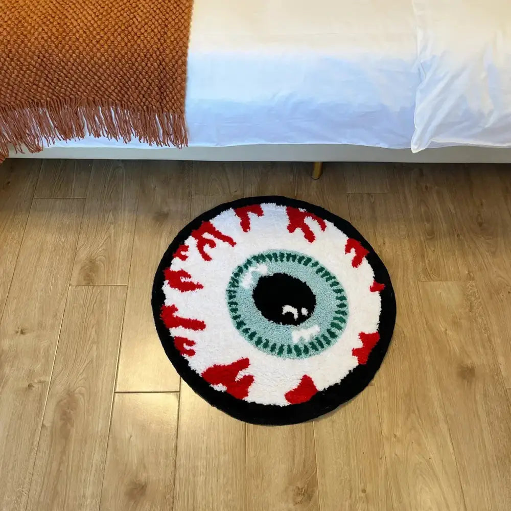 Tapis de bain rond noir et blanc avec un design d’éclaboussures de sang rouge, ressemblant à un œil.