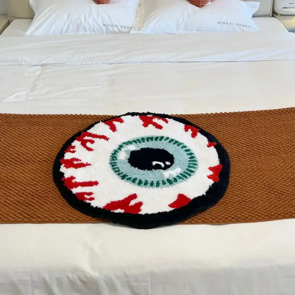 Tapis de bain en forme d’œil rond avec accents rouges et verts, bordure noire, fond blanc, matériau moelleux.
