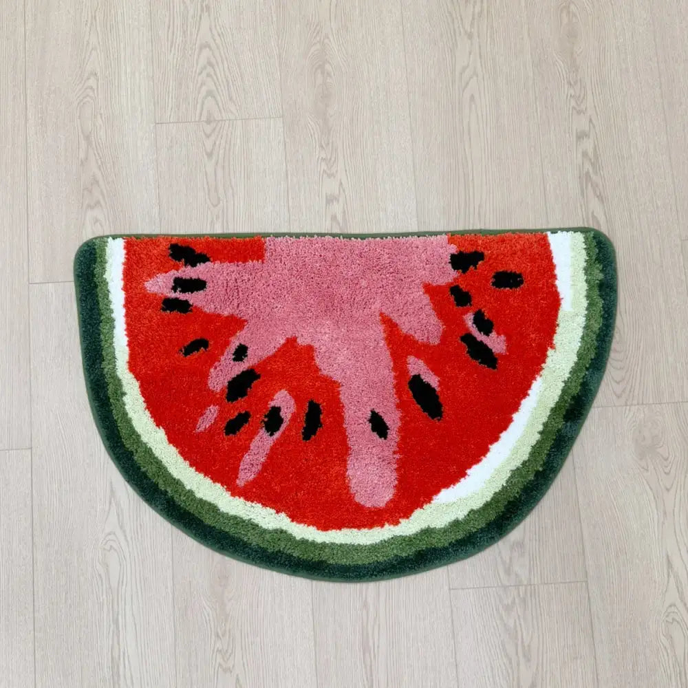 Tapis de bain tranche de pastèque aux teintes vives rouge, vert et rose sur un sol en bois.