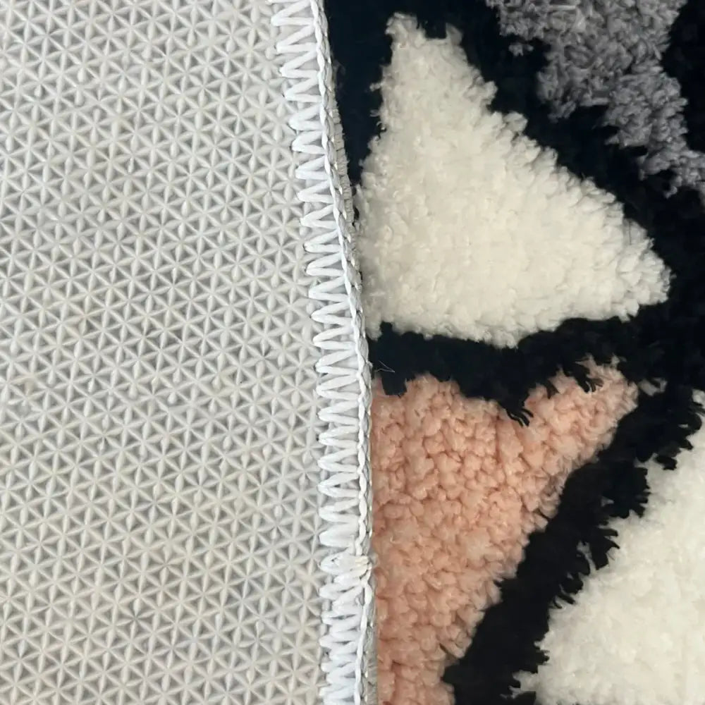 Un tapis moelleux et texturé avec un motif géométrique en tons noir, blanc et rose doux.