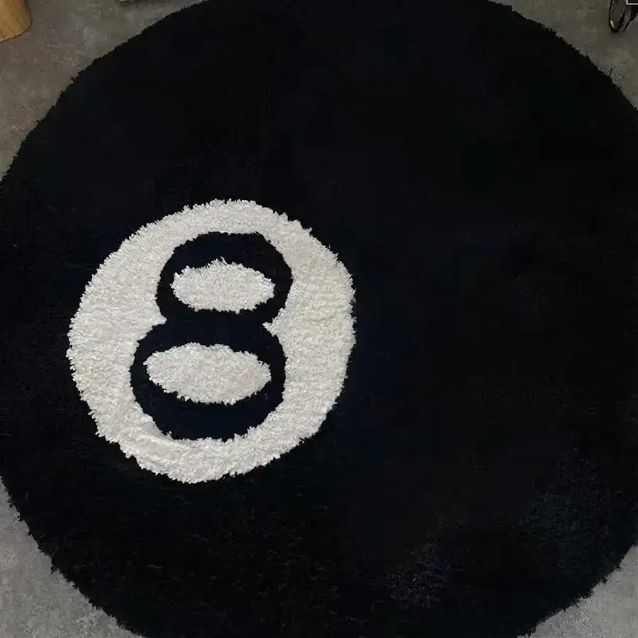 Tapis rond circulaire en peluche noire avec un motif blanc du chiffre huit duveteux au centre.