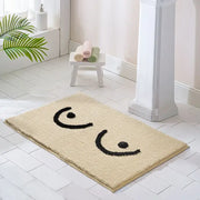 Tapis de bain en peluche beige orné d’un design de visage brodé noir ludique.