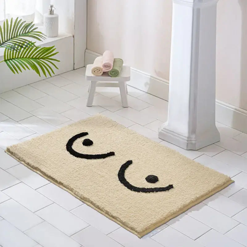 Tapis de bain en peluche beige orné d’un design de visage brodé noir ludique.