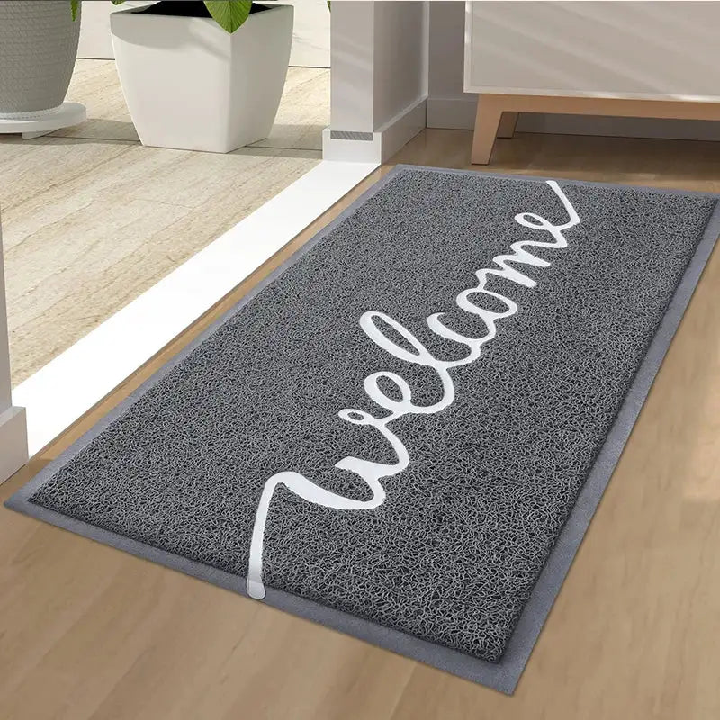 Paillasson de bienvenue avec ’welcome’ en cursif blanc sur fond gris, surface texturée adaptée à un usage intérieur.