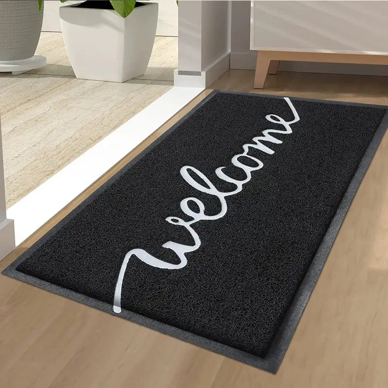 Paillasson de bienvenue avec « welcome » en cursif en blanc sur fond noir, surface texturée adaptée à un usage intérieur ou extérieur.