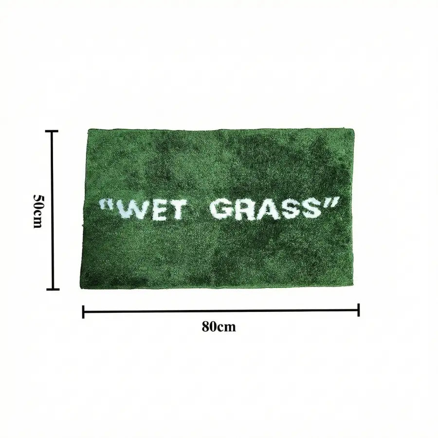Tapis de bain en peluche verte avec ’herbe mouillée’ brodée en blanc.
