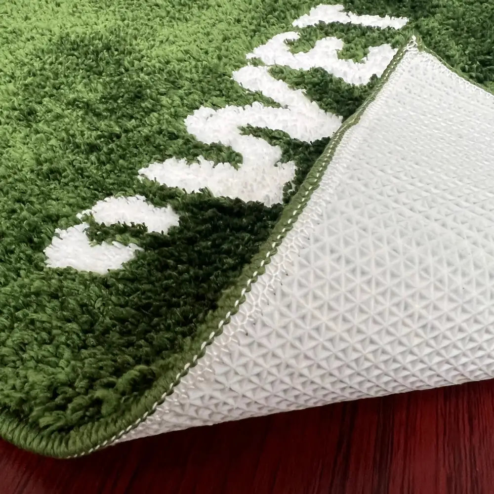 Tapis de bain en peluche verte avec lettrage brodé blanc et dos en caoutchouc texturé.